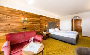 Gemütliches Hotelzimmer mit Doppelbett, rotem Sessel und Holzdekoration, perfekt für entspannte Urlaubstage, zentrale Lage, Komfort und stilvolles Ambiente, ideal für Erholung und Aufenthalt.