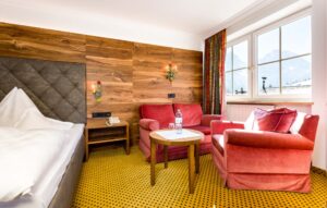 Geräumiges Hotelzimmer mit gemütlicher Sitzecke, Holzdekoration und Bergblick, ideal für einen entspannenden Aufenthalt in den österreichischen Alpen.
