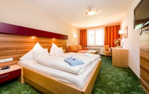 Gemütliches Hotelzimmer mit Doppelbett, TV, Schreibtisch, Sitzbereich, Balkon und Panoramablick in einer österreichischen Unterkunft.
