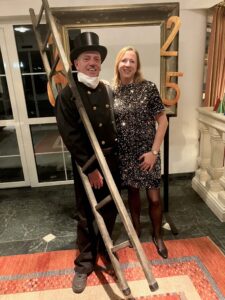 Lagerfeuer- und Lagerfeuer-Foto, auf dem ein Mann im schwarzen Zirkus- oder Zaubererkostüm und eine Frau in einem schwarzen Paillettenkleid stehen, in einer festlichen Umgebung.